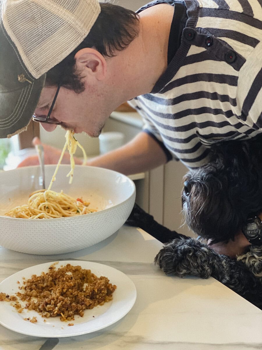 Lionel qui mange des spaghetti direct du bol avec chien qui regarde
