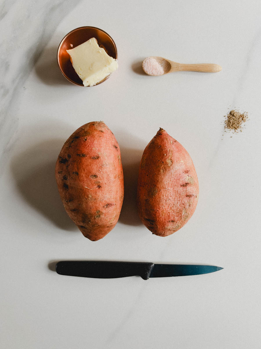 2 patates douces avec couteau, bol de beurre, sel et poivre sur comptoir blanc marbré