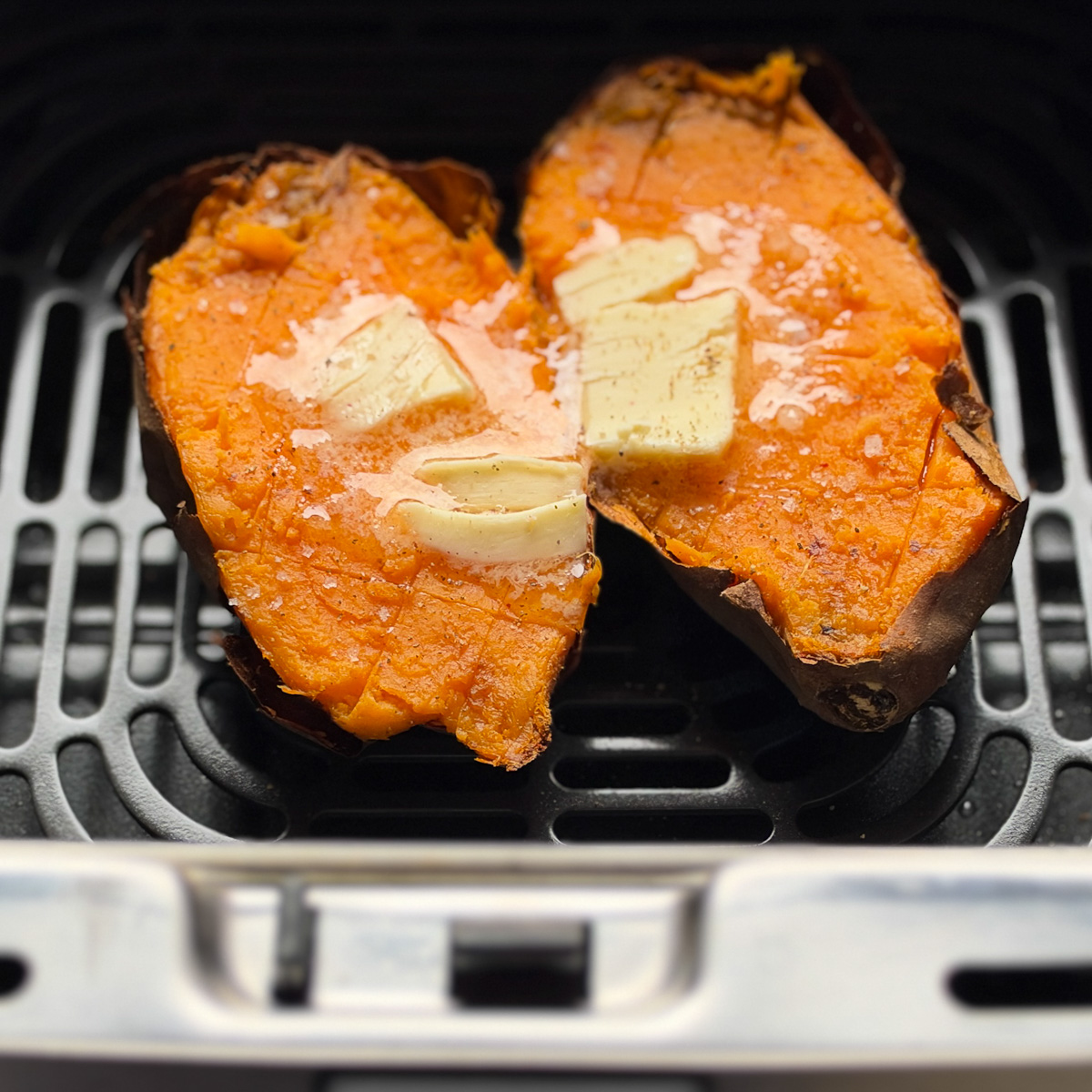 patate douce ouverte au centre avec carré de beurre sur chaque moitié, flocons de sel dans le panier du air fryer