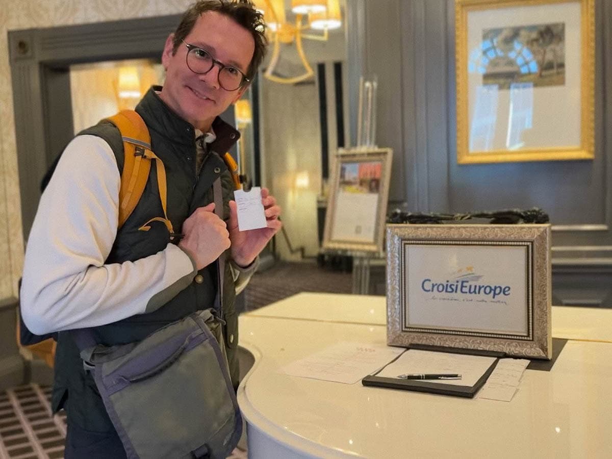 Lionel qui tient sa carte de chambre devant piano avec affiche CroisiEurope dans le lobby de l'hôtel