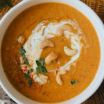 soupe de lentilles corail et lait de coco dans bol blanc, cuillère à côté sur table de bois