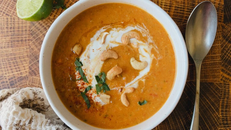 soupe de lentilles corail et lait de coco dans bol blanc, cuillère à côté sur table de bois