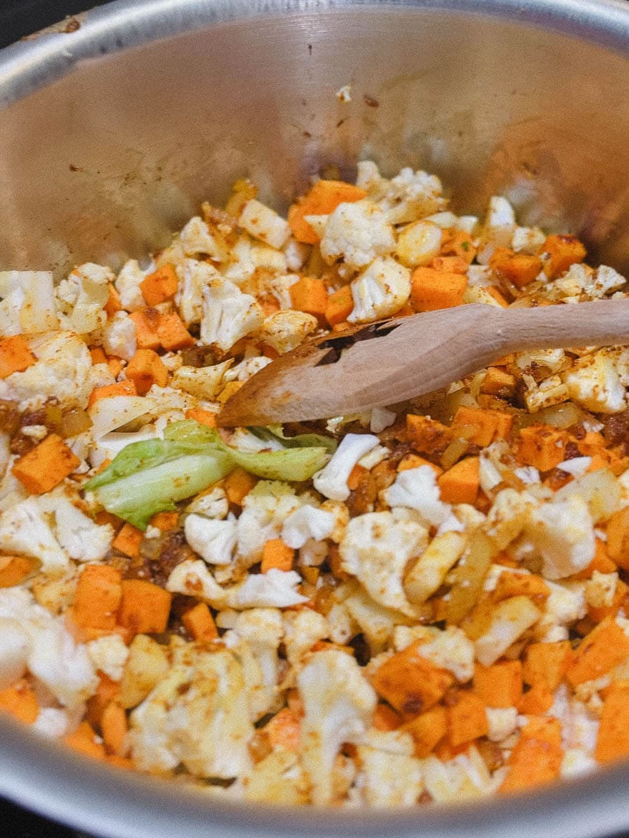 chou fleur, patate sucrée, oignon et épice dans casserole avec cuillère en bois