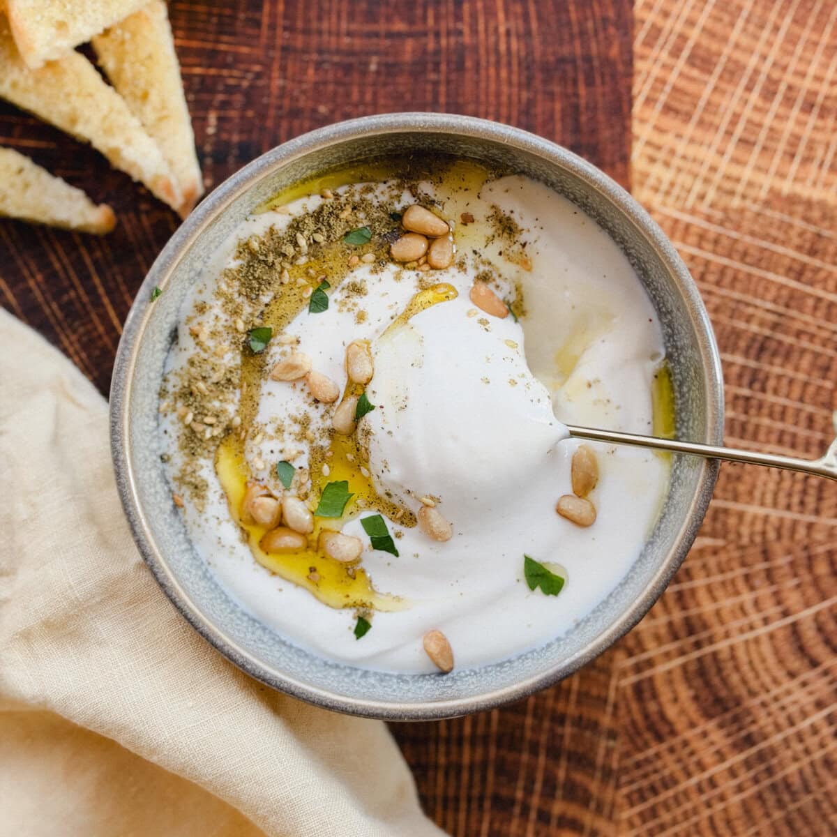 tartinade au feta fouetté dans un bol avec cuillère dorée, garni de zaatar, huile d'olive et pignon sur planche de bois
