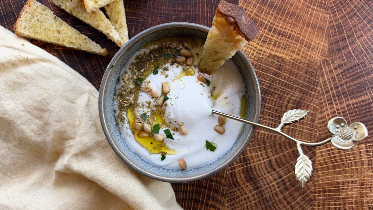 tartinade au feta fouetté dans un bol avec cuillère dorée et crouton de pain sur planche de bois