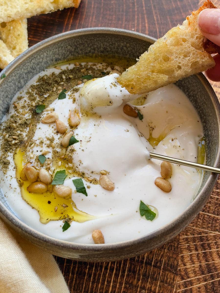 main qui tient un croûton de pain trempé dans tartinade de feta fouetté