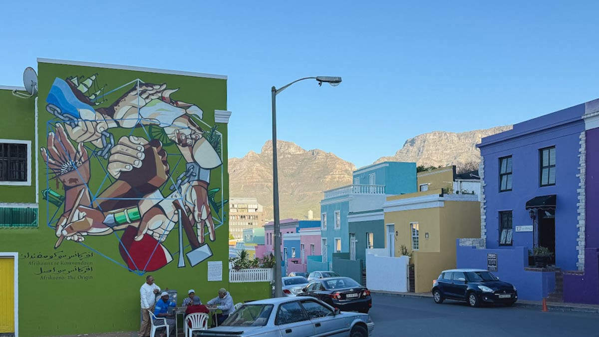 Hommes jouant aux cartes sous un building avec murale à bo-kaap