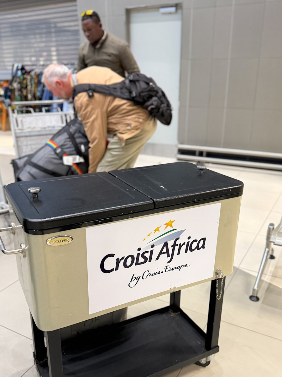 Guide portant valise a l'aeroport devant kiosque CroisiAfrica