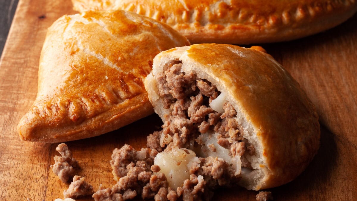 Pochettes-tourtières au air fryer dorées sur une planche de bois, une coupée pour montrer la garniture de bœuf haché et de pomme de terre