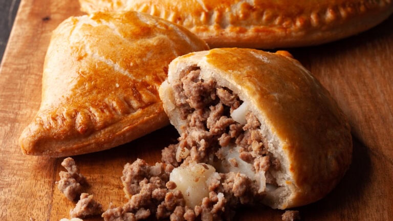 Pochettes-tourtières au air fryer dorées sur une planche de bois, une coupée pour montrer la garniture de bœuf haché et de pomme de terre